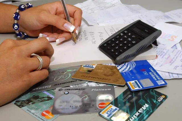  Mujer sacando cuentas con sus tarjetas de crédito y calculadora sobre la mesa. Foto: Andina   