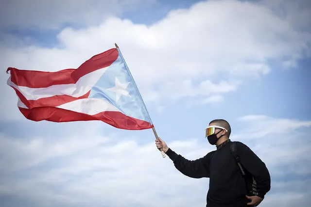 Puerto Rican reggaeton singer Bad Bunny waves a Puerto Rican flag as he takes part of a demonstration demanding Governor Ricardo Rossello's resignation in San Juan, Puerto Rico on July 17, 2019. - Thousands marched in Puerto Rico for a fifth day on Wednesday demanding the resignation of Governor Ricardo Rossello, following corruption accusations and the leak of text chats in which he made sexist and homophobic remarks. (Photo by eric rojas / AFP) / �The erroneous mention appearing in the metadata of this photo by Eric Rojas has been modified in AFP systems in the following manner: [singer Bad Bunny] instead of [singer Bud Bunny]. Please immediately remove the erroneous mention[s] from all your online services and delete it (them) from your servers. If you have been authorized by AFP to distribute it (them) to third parties, please ensure that the same actions are carried out by them. Failure to promptly comply with these instructions will entail liability on your part for any continued or post notification usage. Therefore we thank you very much for all your attention and prompt action. We are sorry for the inconvenience this notification may cause and remain at your disposal for any further information you may require.�