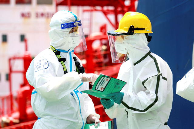 Policía (izquierda) con equipo de protección explica la información de prevención de pandemias para luchar contra la propagación del COVID-19 a un trabajador en el puerto de Nanjing, en la provincia oriental china de Jiangsu. Foto: AFP