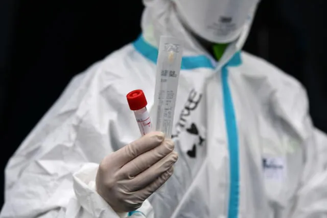 A hospital employee wearing protection mask and gear shows a swab, a cotton wab for taking mouth specimen, used at a temporary emergency structure set up outside the accident and emergency department, where any new arrivals presenting suspect new coronavirus symptoms will be tested, at the Brescia hospital, Lombardy, on March 13, 2020. (Photo by Miguel MEDINA / AFP)