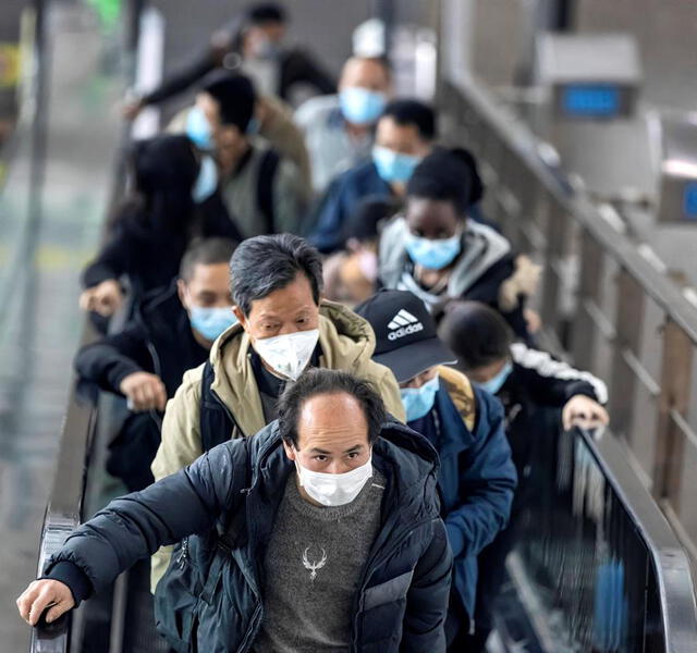 Personas con máscaras suben por una escalera mecánica en la estación de tren de alta velocidad en China. Foto: EFE.